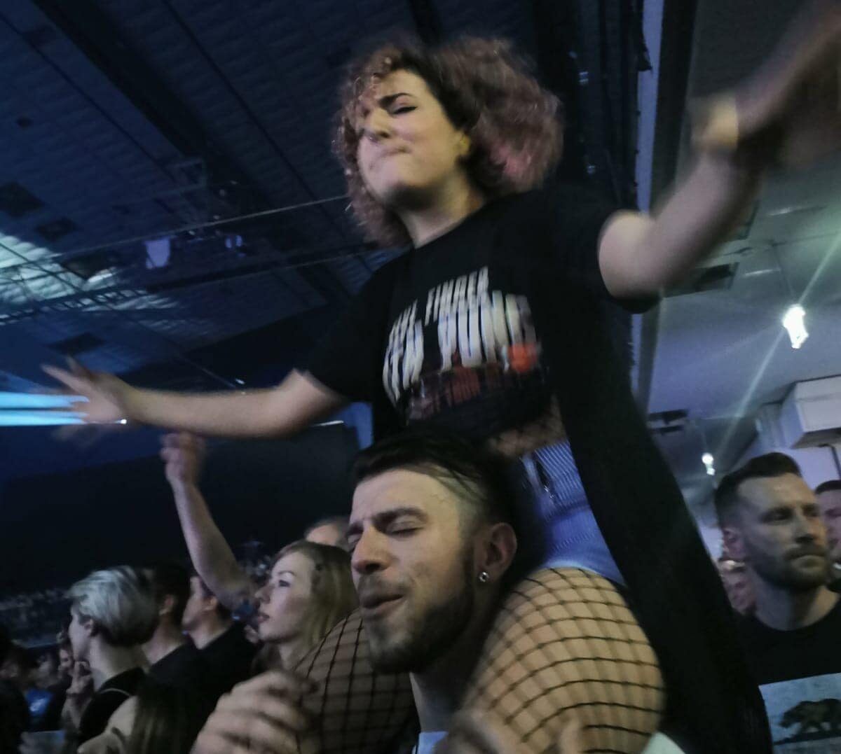 Eine kleine Frau bei einem Konzert, auf den Schultern eines Mannes