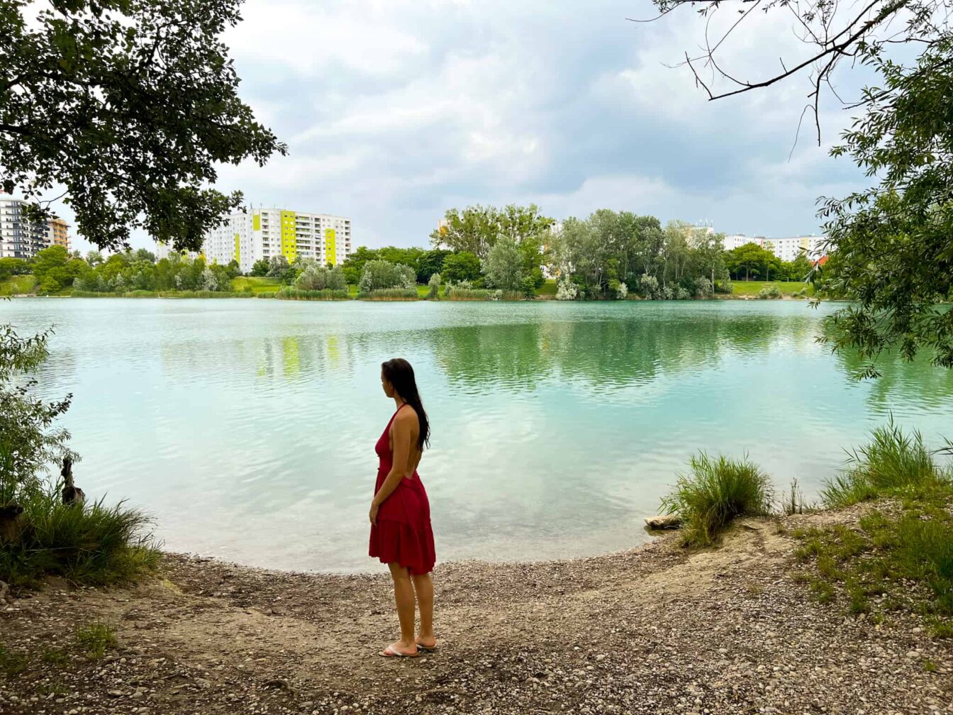 Frau in rotem Kleid steht auf dem Kiesstrand des Badeteichs Hirschsstetten in Wien