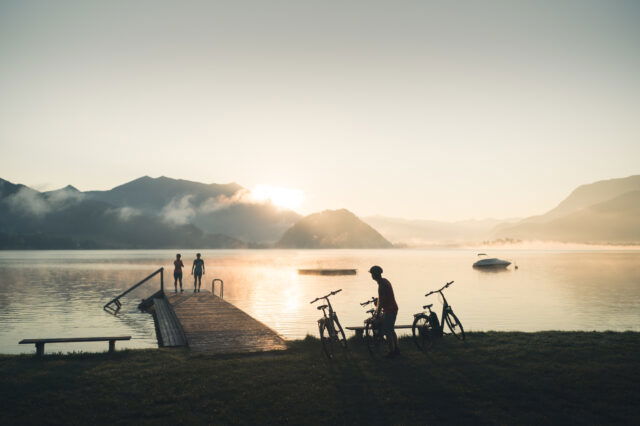 Foto Oberösterreich Tourismus/Wolfgangsee/Moritz Ablinger: Radler im Sonnenuntergang am Steg des Gemeindebades Gschwendt in Strobl am Wolfgangsee im Salzkammergut.