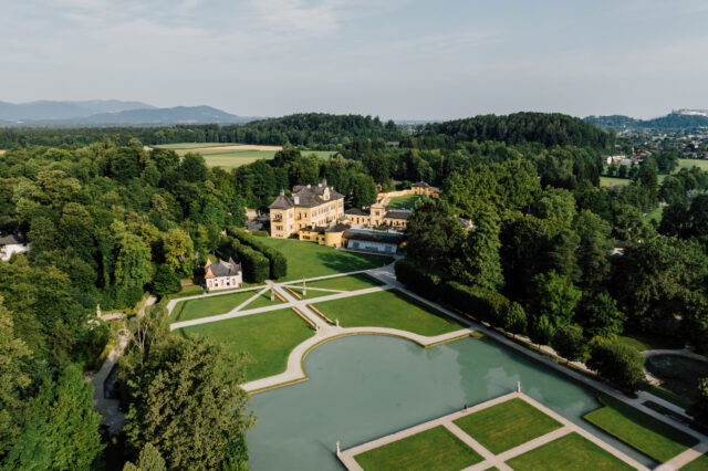 Panoramaaufnahme von Schloss Hellbrunn in Salzburg mit prächtiger Parkanlage, barockem Lustschloss und Wasserspielen, eingebettet in die grüne Naturlandschaft.