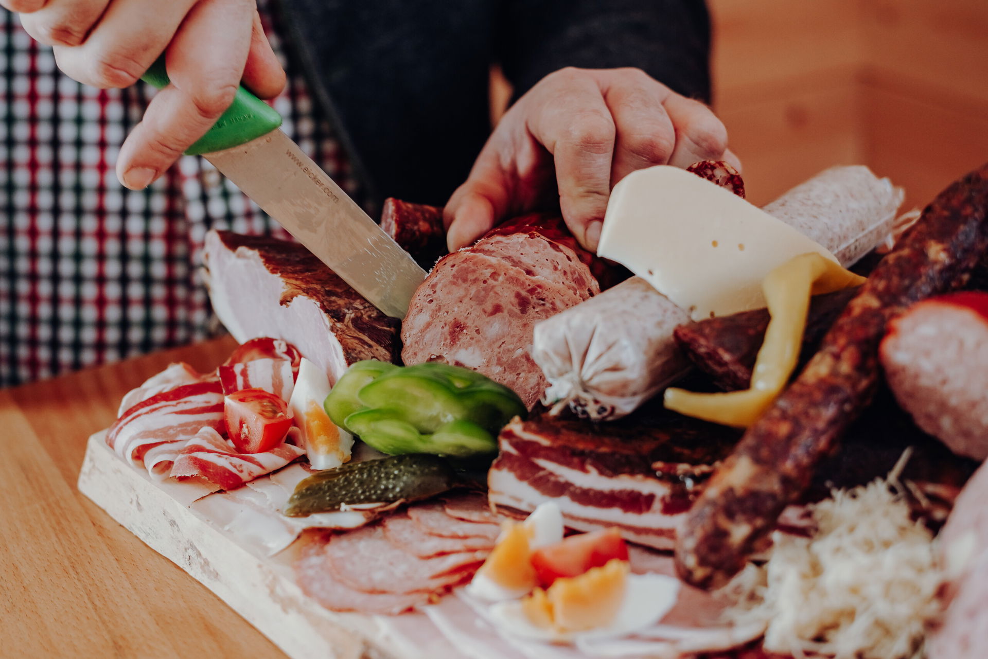 Bild von einer steirischen Brettljause, eine Hand im Bild hält eine Salami fest, die andere schneidet gerade eine Scheibe herunter.