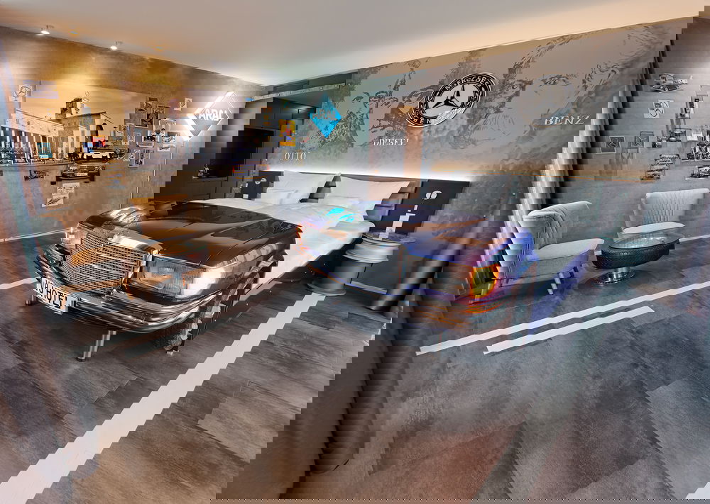 Hier sieht man ein Hotelzimmer, in dem ein Bett steht, dass in ein Auto hineingebaut wurde.