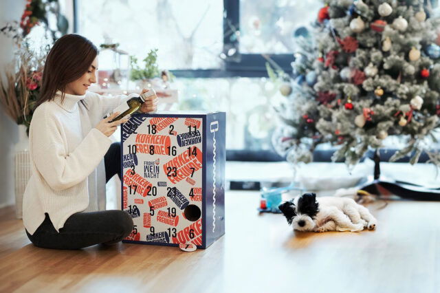 Korkenfreunde: Alkohol-Adventkalender mit Wein, Frau mit Hund packt ihn aus