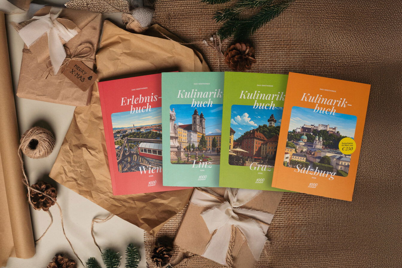 1000things Erlebnisbuch Wien sowie Kulinarikbücher für Linz, Graz und Salzburg, stimmungsvoll arrangiert mit Geschenkpapier, Tannenzweigen und Weihnachtsdeko – ideales Weihnachtsgeschenk für Kulinarik- und Erlebnisfans.