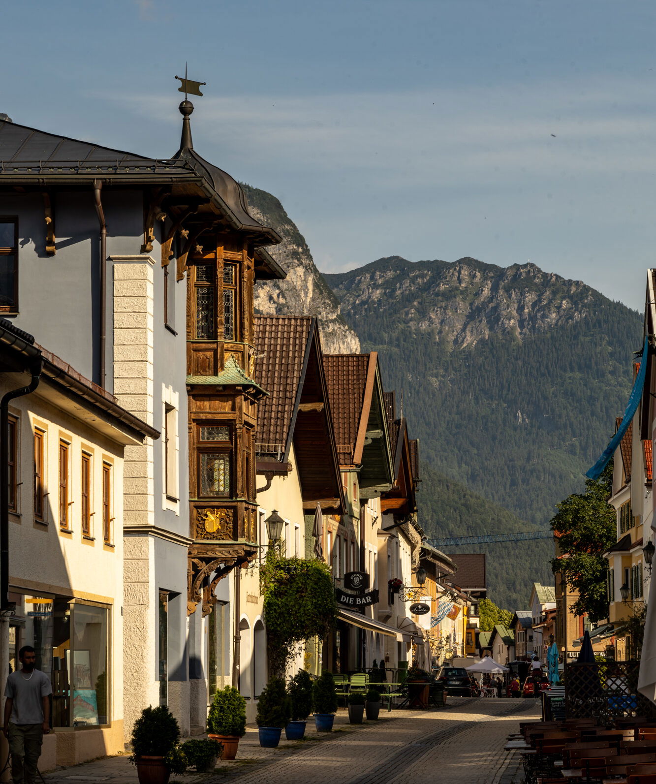 Ludwigstraße in Garmisch-Partenkirchen bei Sonnenschein – historische Häuser mit Holzverzierungen, gemütliche Straßencafés und Blick auf die umliegenden Alpen