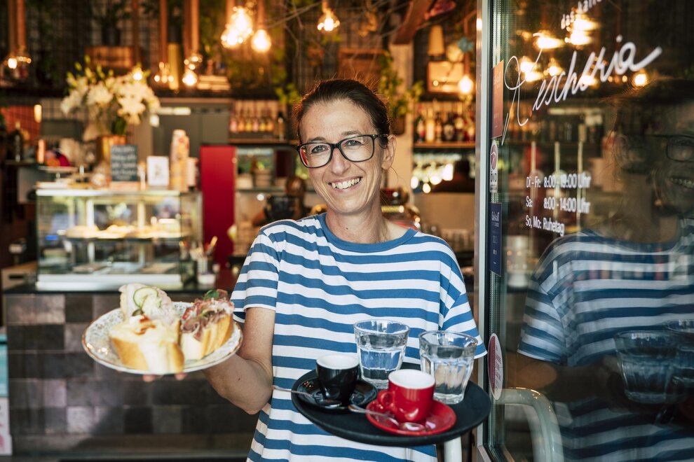 Person steht mit Brötchen und Kaffee in offener Kaffeehaus-Tür
