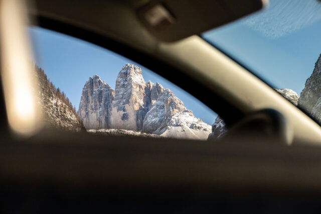 Im Vordergrund ein Auto, durch das Fenster sieht man die Drei Zinnen, das Wahrzeichen von Südtirol