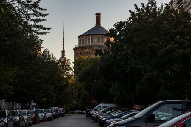 Baumbestandene Berliner Straße mit parkenden Autos in der Rykestraße in Prenzlauer Berg, im Hintergrund der Wasserturm und der Fernsehturm im Abendlicht.