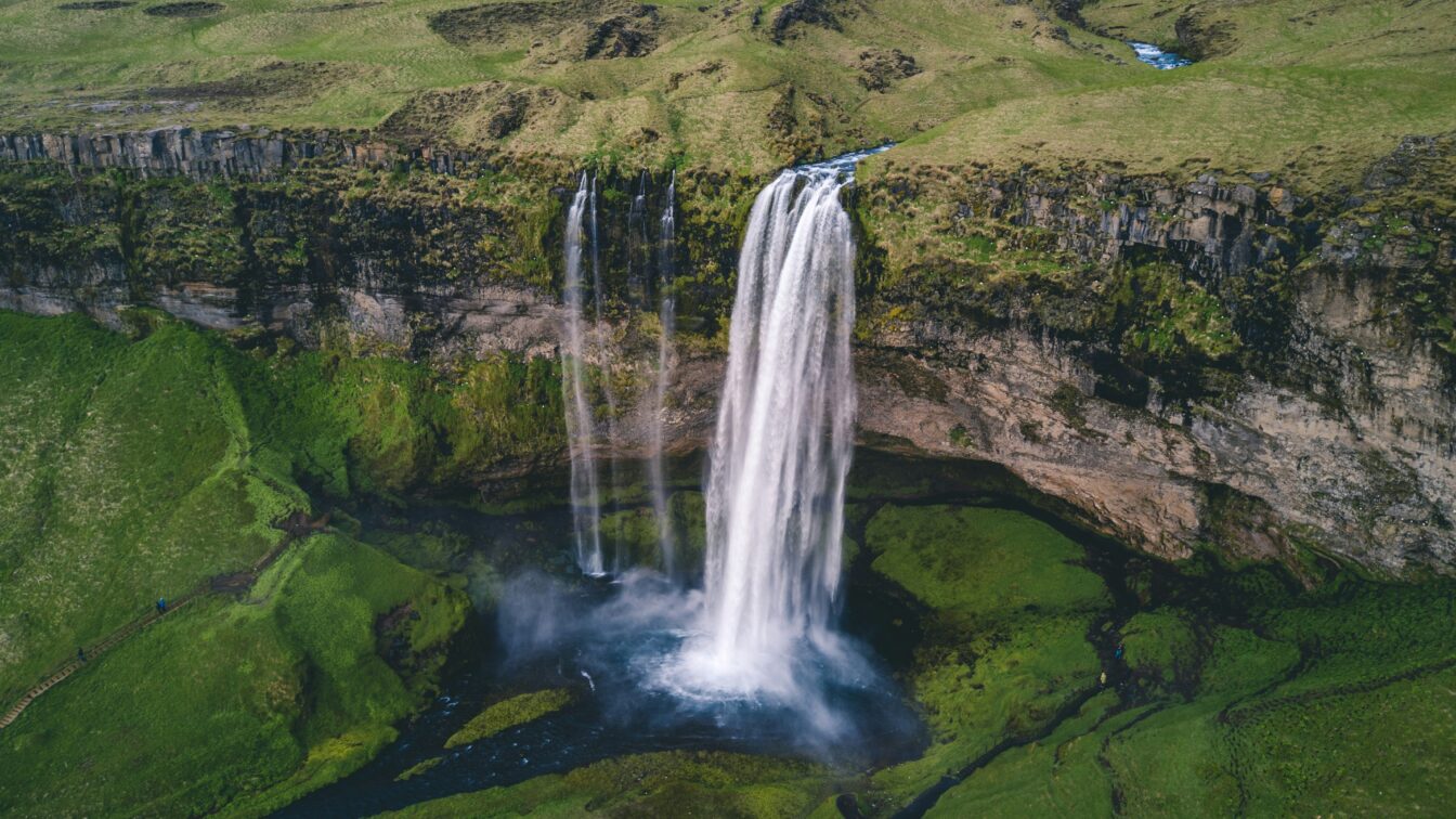 (c) Lucas Davies | Unsplash Grüne Wiesen in Island mit Wasserfall