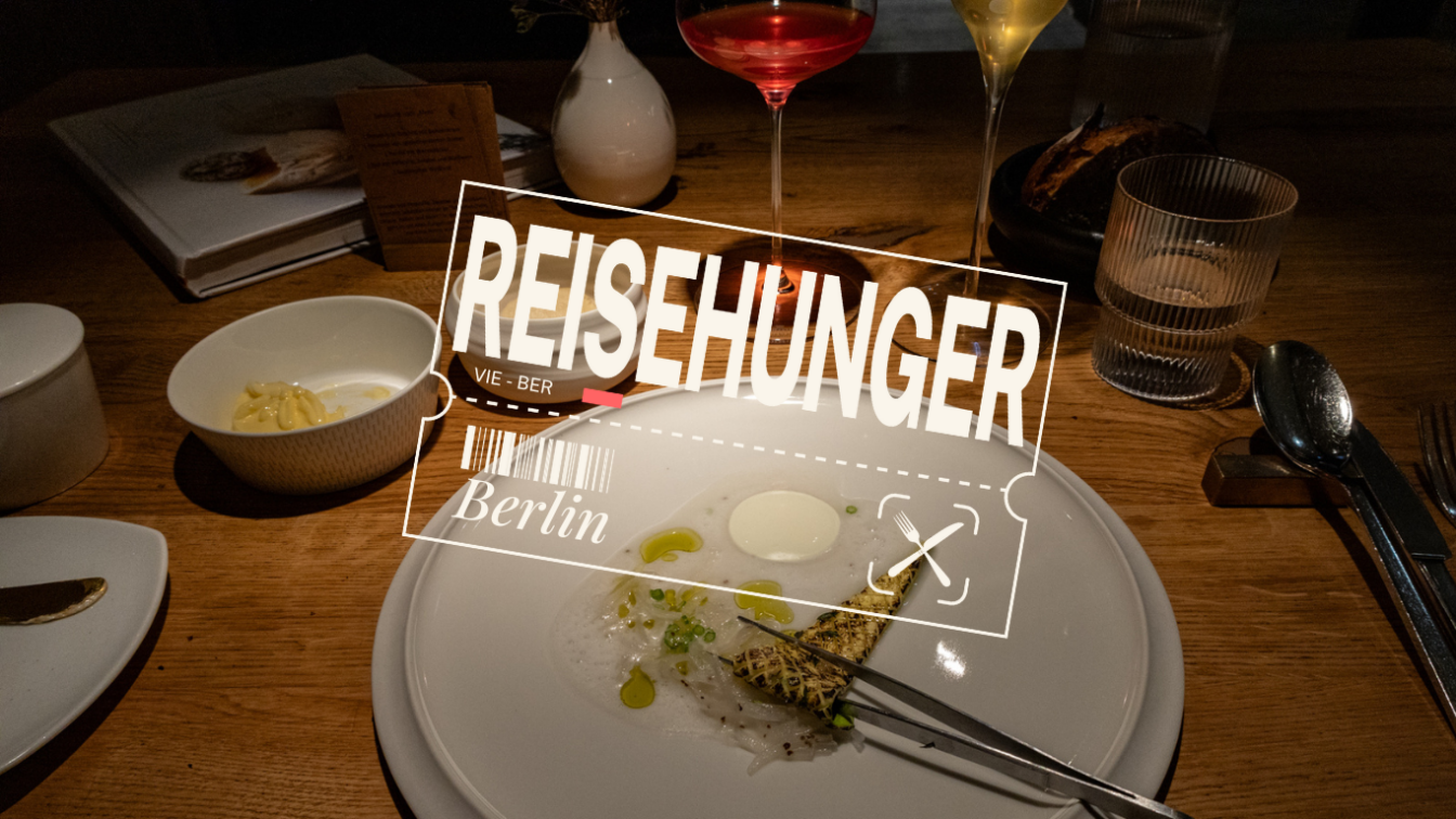 (c) Sonja Koller | 1000things Dieses Bild zeigt eine fein gedeckte Restaurant-Tafel im Restaurant Horváth in Kreuzberg, Berlin. Im Vordergrund befindet sich ein elegantes Gericht auf einem weißen Teller – dünn geschnittene Fischscheiben mit grünen Öltropfen, einer Sauce und einem gegrillten Stück Gemüse oder Brot. Ein Messer und eine Gabel liegen auf dem Teller. Links daneben steht eine Schale mit einer gelben Creme oder Butter. Im Hintergrund sind ein Brotteller, Gläser mit Wasser, Weiß- und Rotwein, sowie ein Buch mit einer Speisekarte zu sehen. Der Holztisch verleiht der Szene eine gemütliche Atmosphäre. Eine digitale Grafik mit dem Schriftzug „REISEHUNGER“ sowie „Berlin“ und einer stilisierten Bordkarte überlagert das Bild, was auf eine kulinarische Reise hinweist.