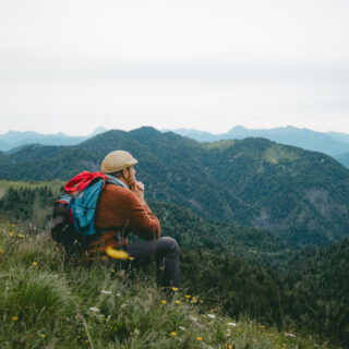 Mann sitzt im Gras in Oberbayern und schaut in die Berge