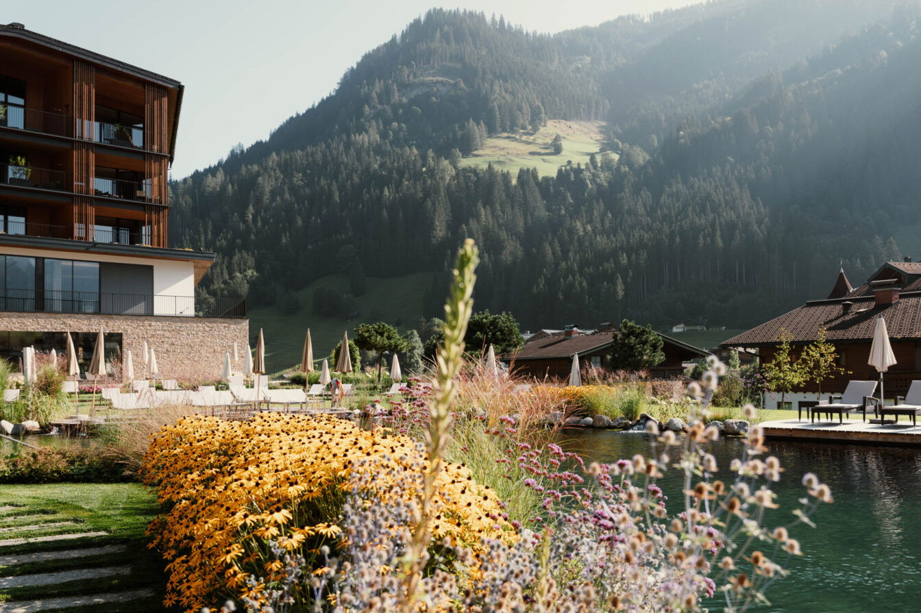 Familienfreundliches Hotel in den österreichischen Alpen mit Naturpool, gemütlicher Sonnenterrasse und blühendem Sommergarten – ideal für einen entspannten Familienurlaub in der Natur