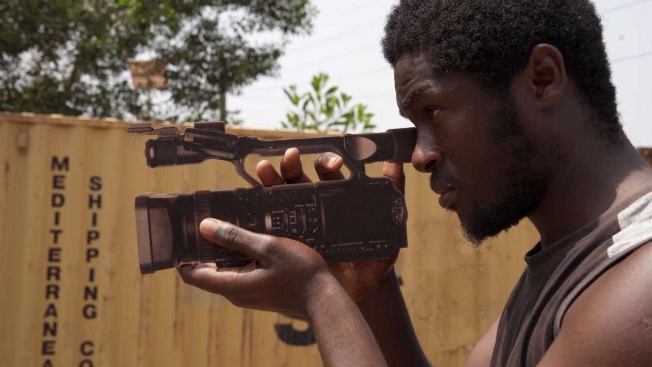 (c) Thierno Souleymane Diallo „Cimetiere de la Pellicule – The Cemetery of Cinema“ 2023 Ein Mann mit Filmkamera in der Hand.