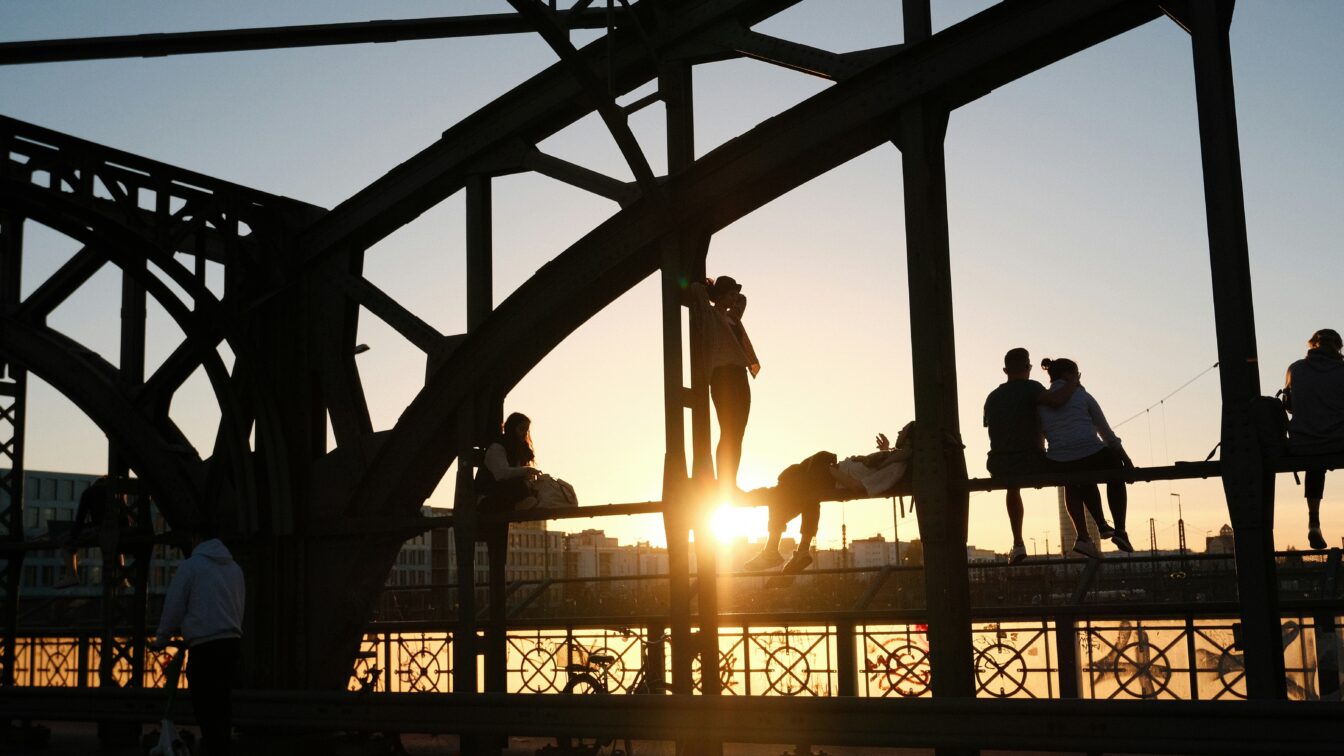 (c) Nk Ni | Unsplash Eine Gruppe von Menschen, die bei Sonnenuntergang auf einer Brücke, der Hackerbrücke in München, stehen
