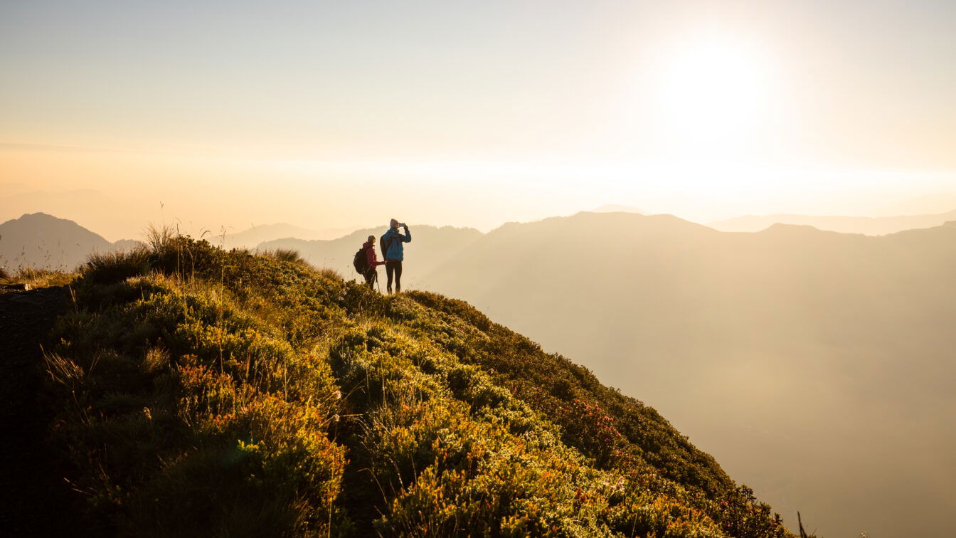 (c) Alpbachtal Tourismus | Shootandstyle Sonnenaufgangswanderung am Wiedersbergerhorn bei Alpbach – zwei Wanderer genießen die goldene Morgenstimmung über dem Alpbachtal in Tirol, mit Blick auf die Bergsilhouetten im Gegenlicht.