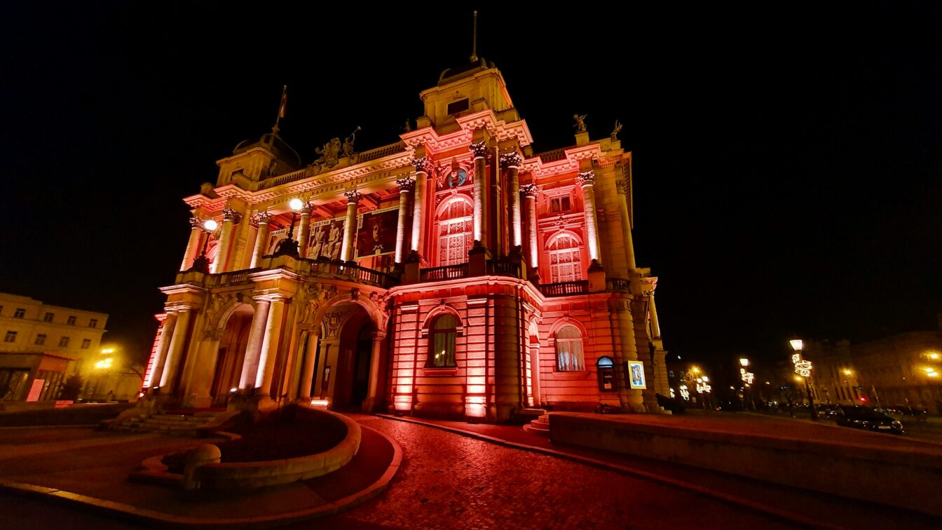 (c) Tomislav Dodig | Unsplash Ein großes, imposantes Gebäude, das rot beleuchtet wird bei Nacht.