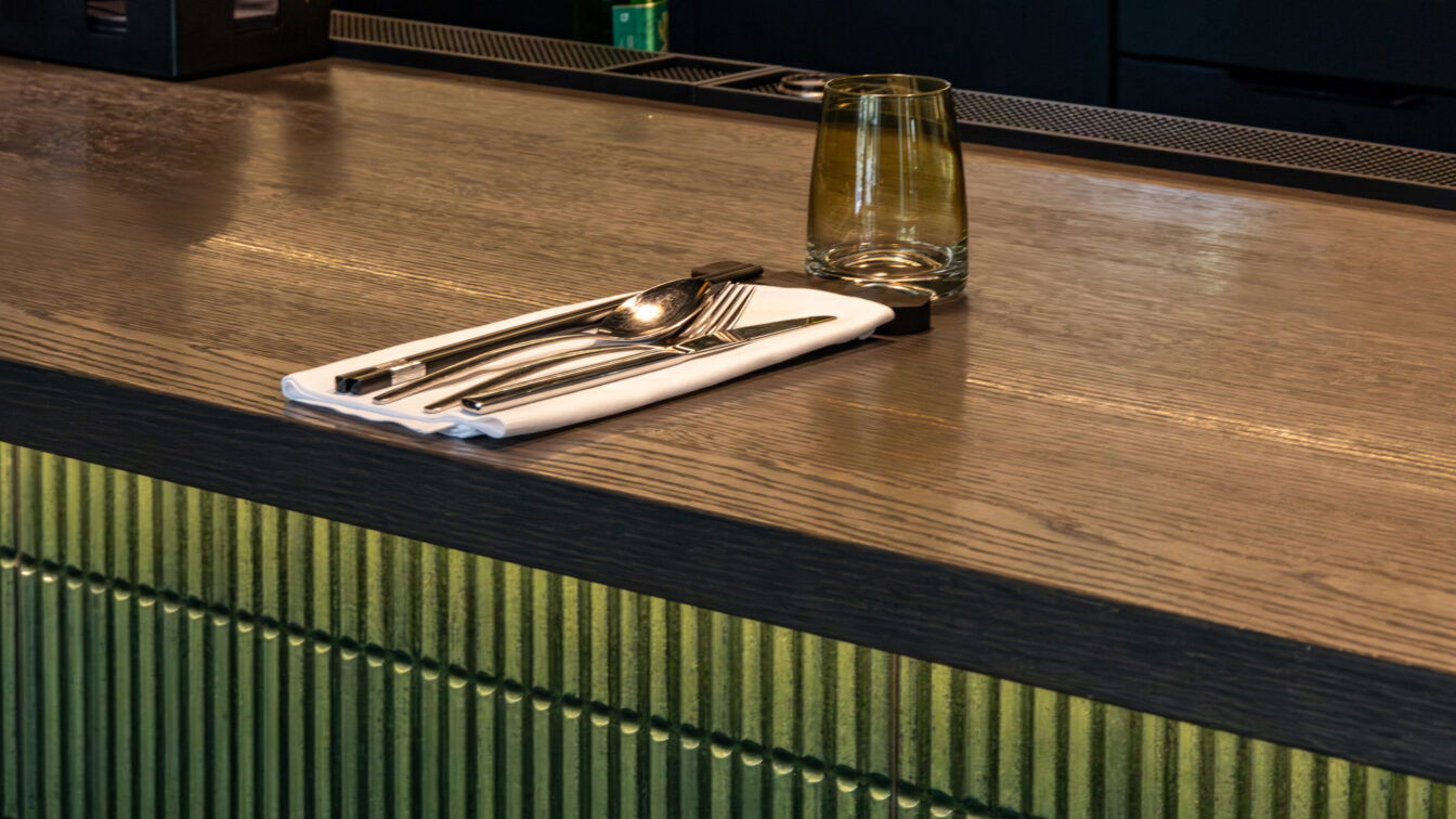 (c) Sonja Koller | 1000things Detailaufnahme eines liebevoll gedeckten Platzes an der Bar im Vina Graz mit Besteck auf weißer Serviette und stilvollem Glas auf dunklem Holztresen.