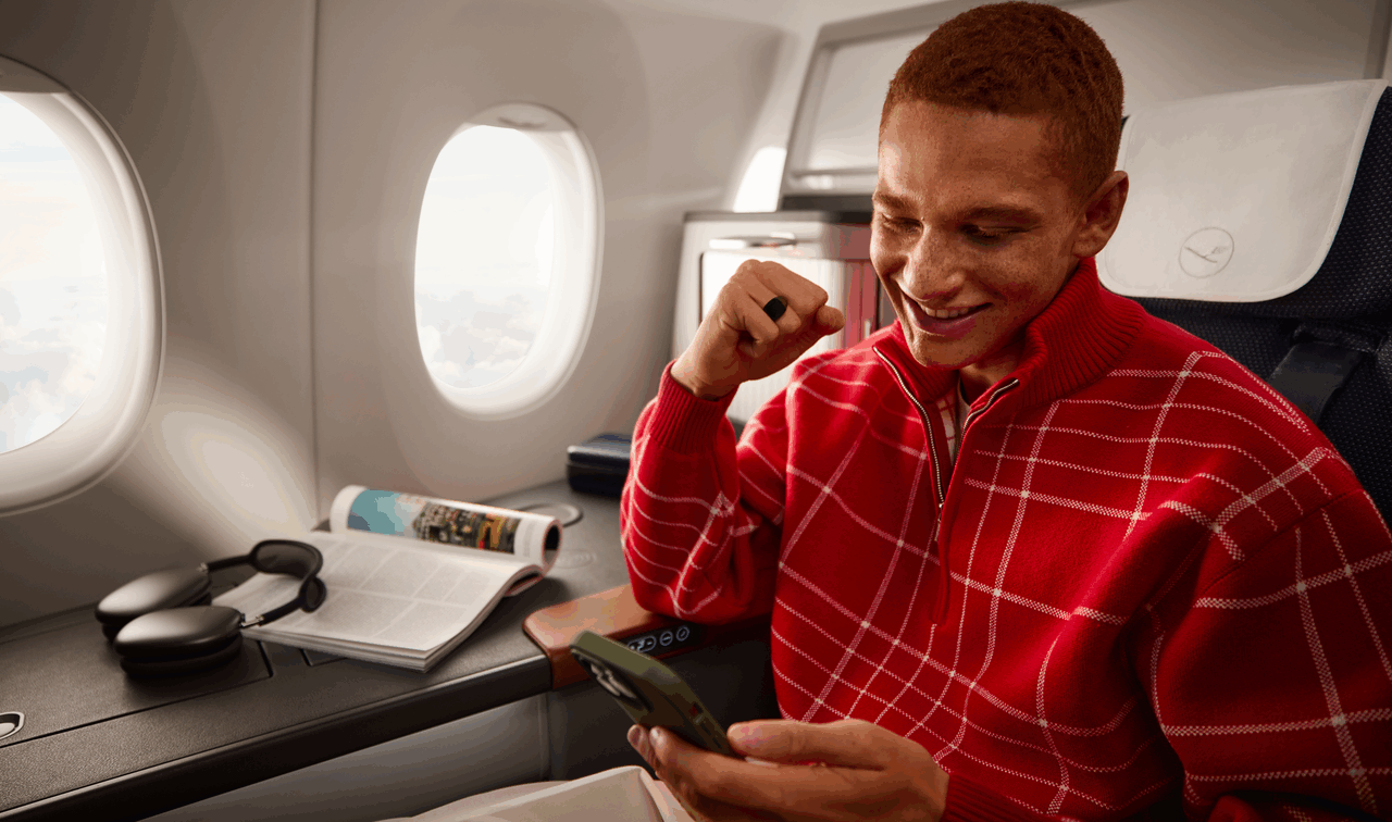 (c) Lufthansa Allegris Ein junger Mann in rotem Pullover, der in der First Class eines Lufthansa Flugzeugs sitzt.