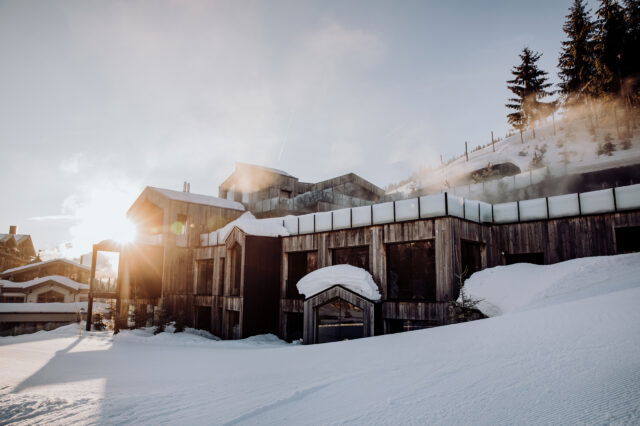 Eine schneebedeckte Landschaft, aus der sich das Naturhotel Forsthofgut erhebt.