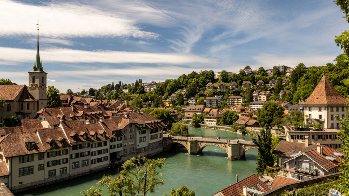(c) Sonja Koller | 1000things Panoramablick auf die Altstadt von Bern in der Schweiz mit der Aare, historischen Häusern mit roten Dächern, der Nydeggbrücke und der Kirche Nydeggkirche – beliebtes Fotomotiv und Ausflugsziel in der UNESCO-Weltkulturerbe-Stadt Bern.