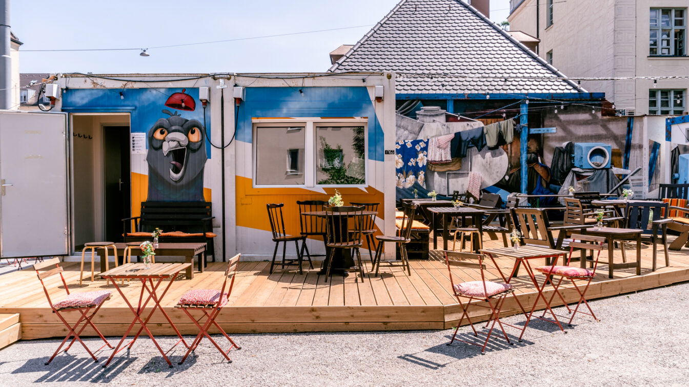(c) Café Steinchen Eine hözerne Terrasse vor einem Café, das mit Graffiti-Kunst verziert ist.