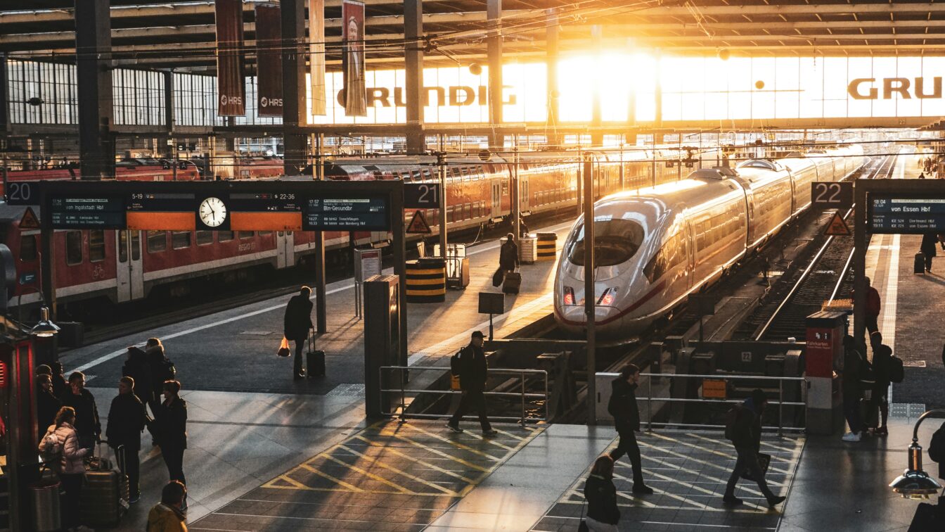 (c) Preston Foster | Unsplash ICE-Zug am Bahnsteig im Hauptbahnhof bei Sonnenaufgang – Reisende auf dem Weg zum Gleis, moderne Bahnreise in Deutschland mit Lichtstimmung im Morgenverkehr.