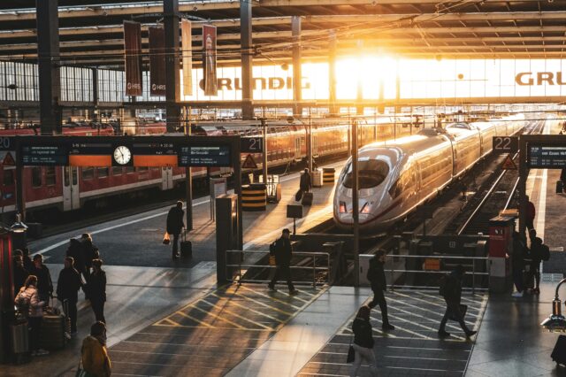 (c) Preston Foster | Unsplash ICE-Zug am Bahnsteig im Hauptbahnhof bei Sonnenaufgang – Reisende auf dem Weg zum Gleis, moderne Bahnreise in Deutschland mit Lichtstimmung im Morgenverkehr.