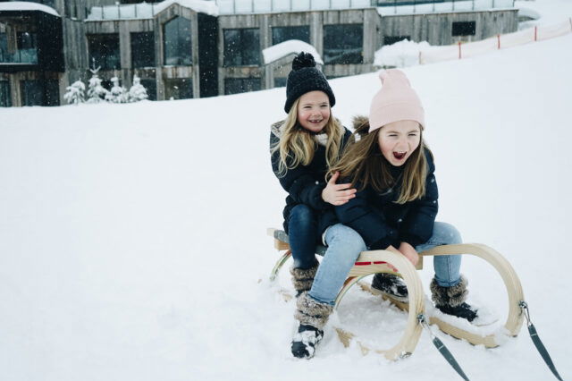 Spaß für die ganze Familie im Naturhotel Forsthofgut. (c) Carina Rabeian Zwei kleine Mädchen auf einem Rodeln, die durch den Schnee gezogen werden.