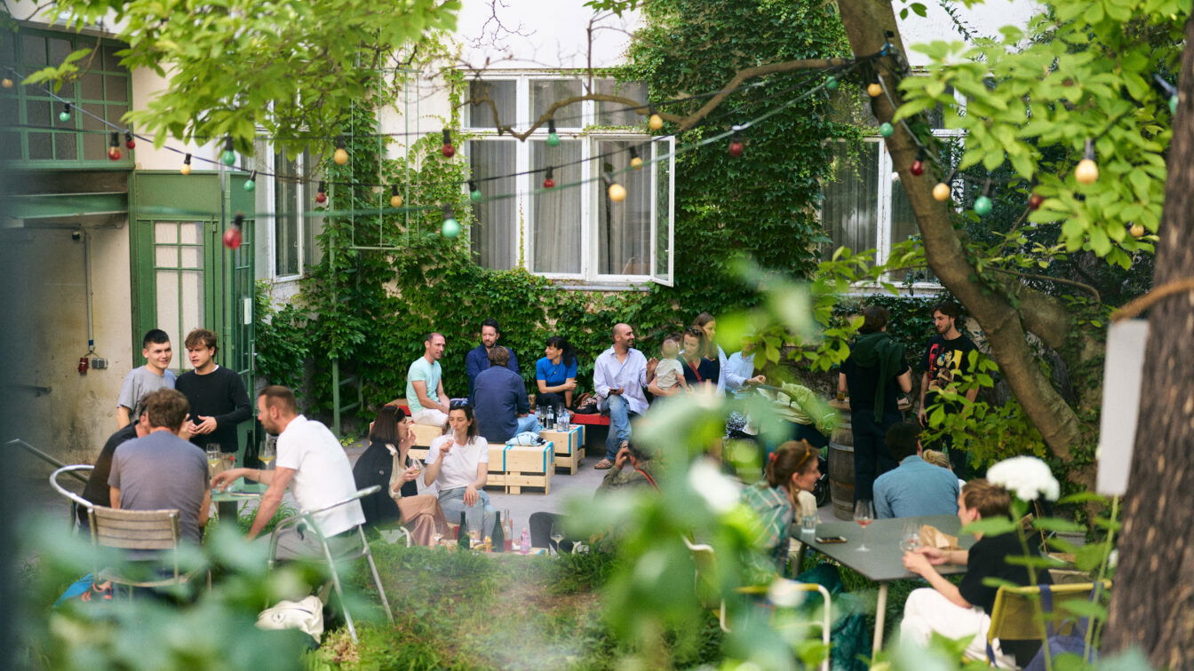 (c) Markus Korenjak Menschen in einem grünen Innenhof, die trinken und essen.