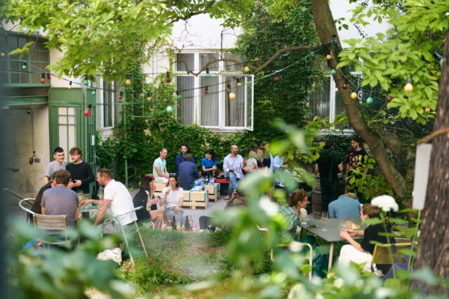 (c) Markus Korenjak Menschen in einem grünen Innenhof, die trinken und essen.