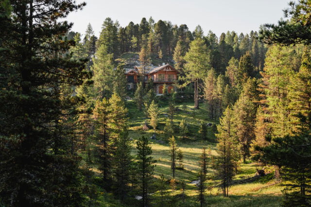 Ein Holzhaus in der Ferne, umgeben von grünem Wald und einem kleinen Bach auf der Turracher Höhe.