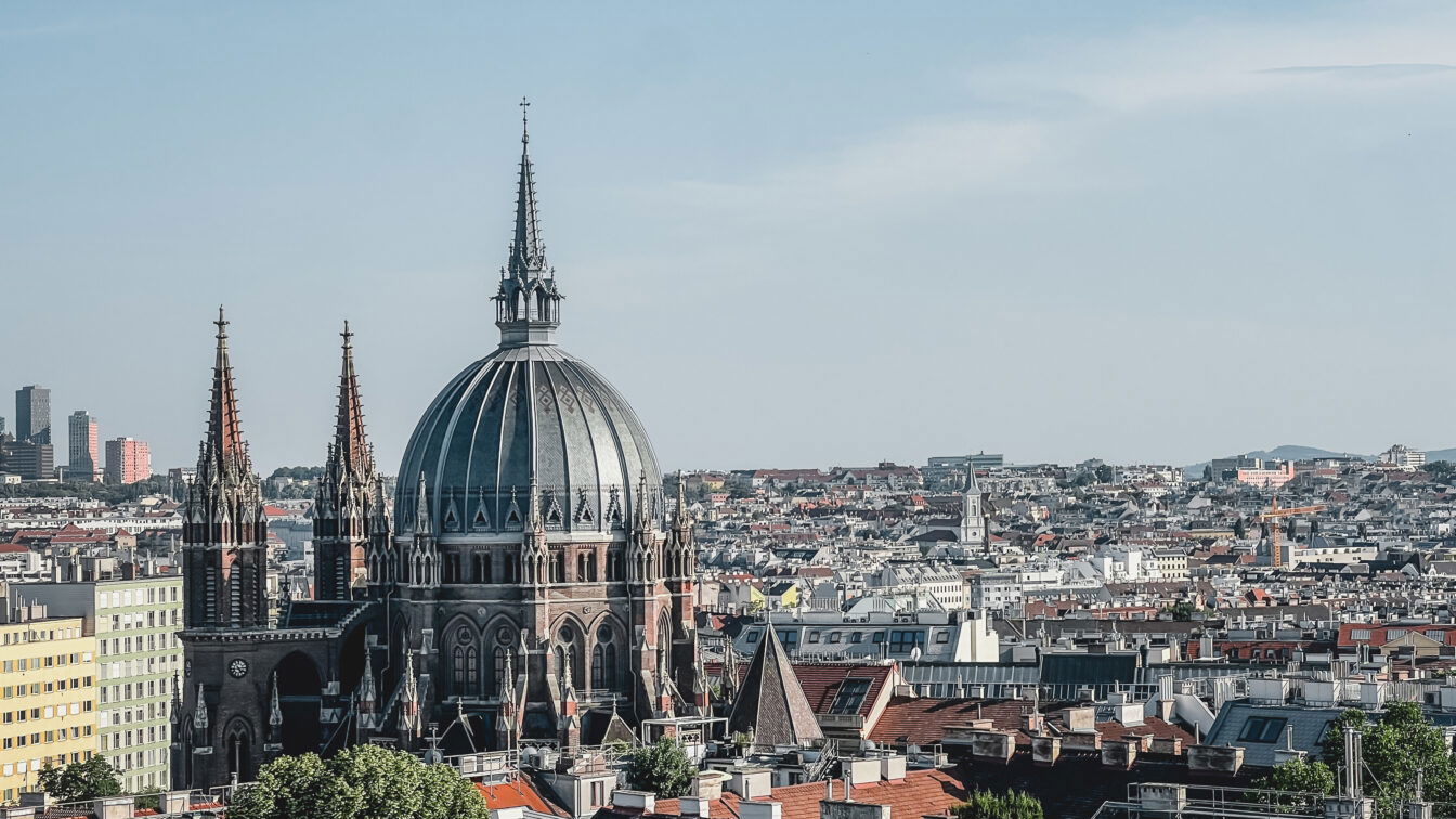 (c) Lilli Wermuth | 1000things Blick über Wien an einem Sommerabend, der die Skyline freigibt und die Kirche Maria vom Siege zeigt.