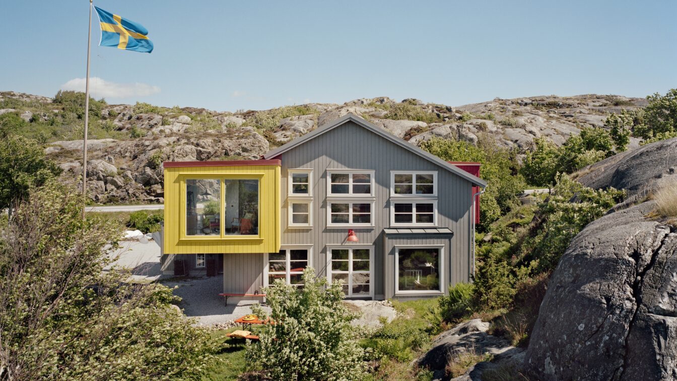 (c) Lådfabriken Modernes Gästehaus Lådfabriken an der schwedischen Westküste – stilvolles Architektenhaus mit farbigen Akzenten inmitten felsiger Landschaft und Natur, mit schwedischer Flagge im Vordergrund.
