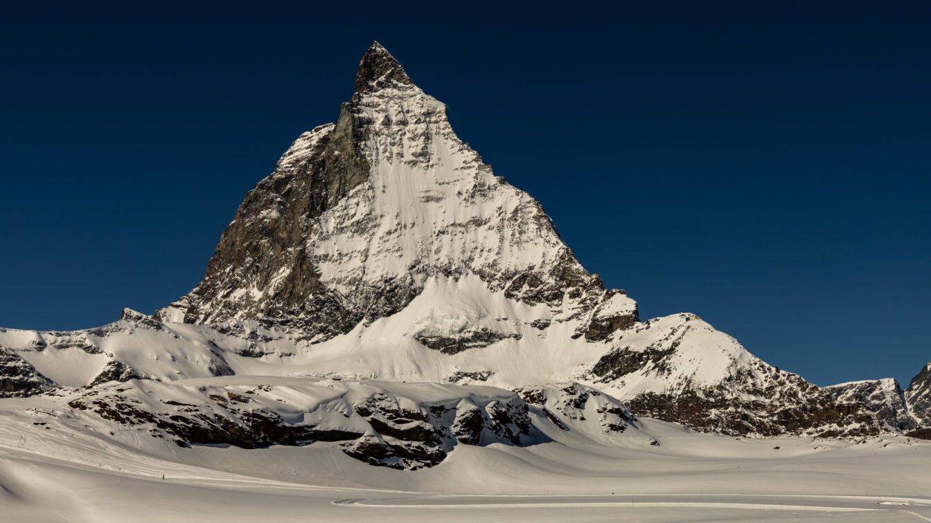 Schneebedecktes Matterhorn vor tiefblauem Himmel in der Schweiz, fotografiert bei klarem Winterwetter. Im Vordergrund eine weite, unberührte Schneelandschaft.