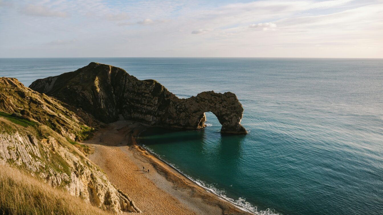 Durdle Door in Wareham, Großbritannien. (c) Pauline Herpel | Unsplash Blick von einer Klippe aus auf eine Felsenformatione, die ins Wasser ragt.