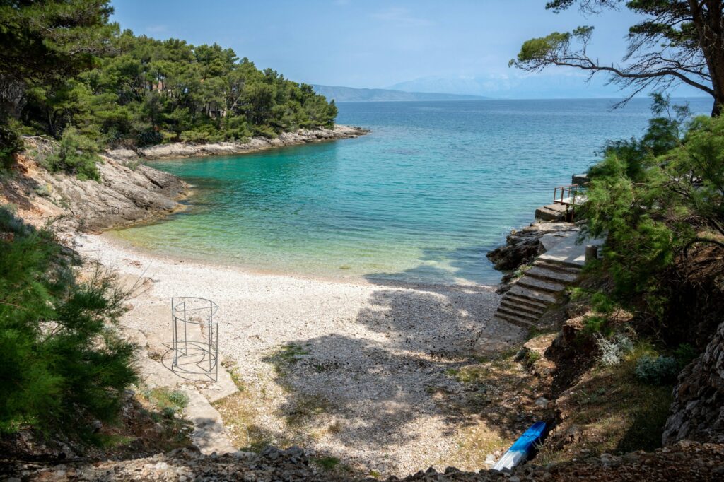 Ein menschenleerer Strand in Kroatien, der umringt von Bäumen türkisblaues Wasser verspricht.