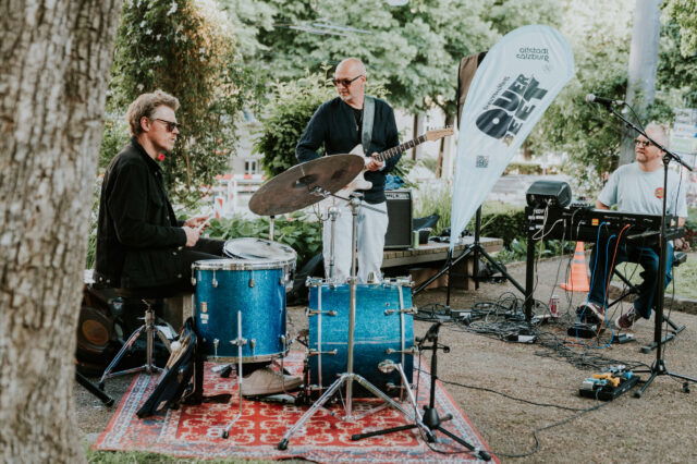 Live-Musik im Schanzlpark Salzburg – Band mit Schlagzeug, Gitarre und Keyboard bei Open-Air-Konzert der Veranstaltungsreihe 'Altstadt Salzburg Über d’Gass', stimmungsvolle Atmosphäre unter freiem Himmel.