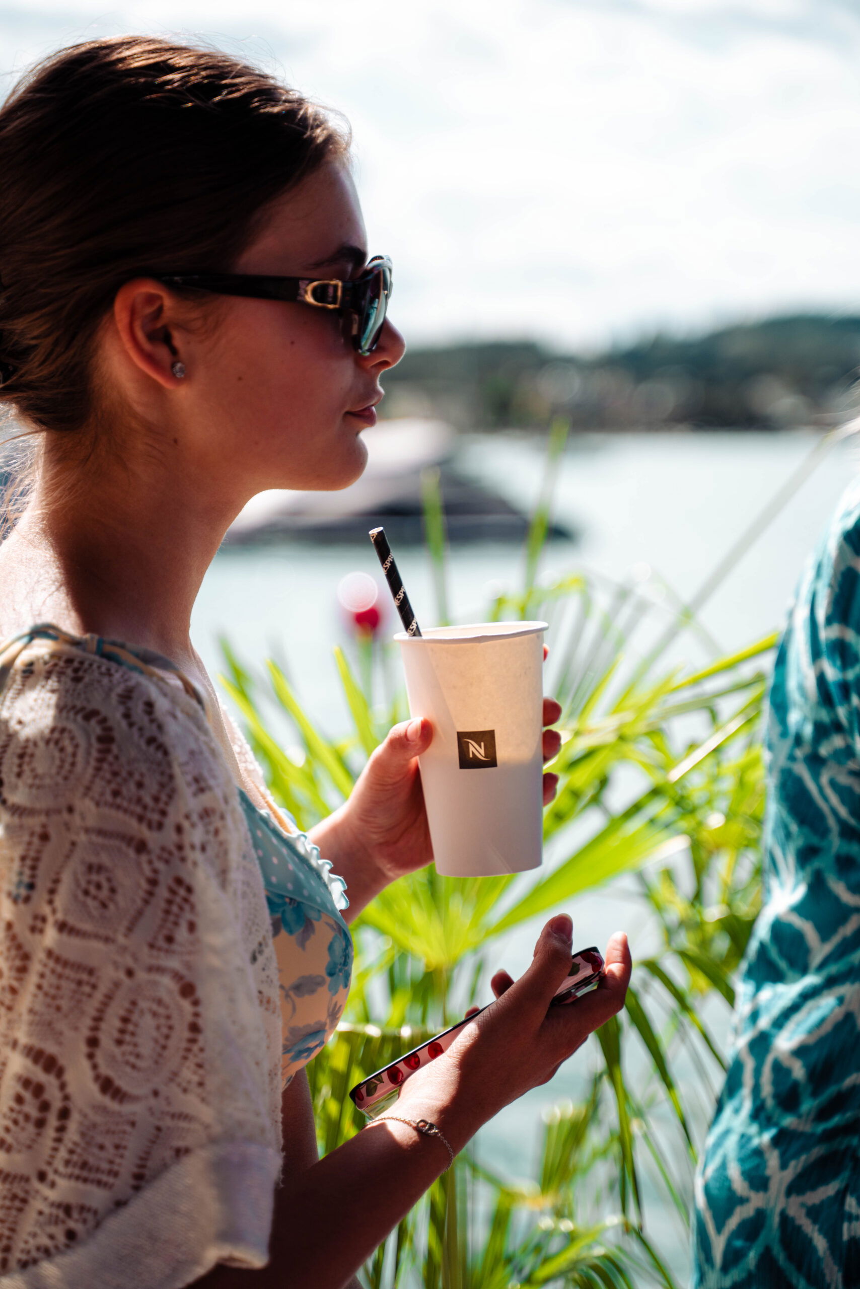 Frau am Wasser im Sommer mit Sonnenbrille und Kaffee-Becher (c) FRB Media | Moritz Scheibenreif