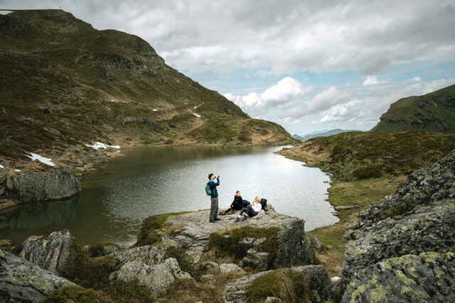 Drei Personen wandern in den Bergen und rasten am Bergsee