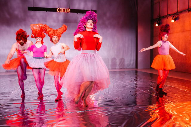 Personen in bunten Kleidern und Röcken in einem Theaterstück
