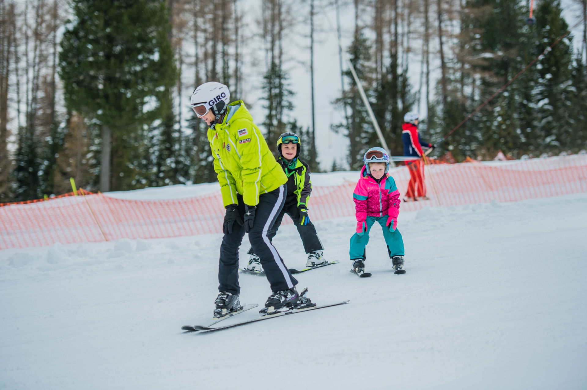 Eine Frau zeigt zwei Kindern das Skifahren beim Winterurlaub in der Steiermark.