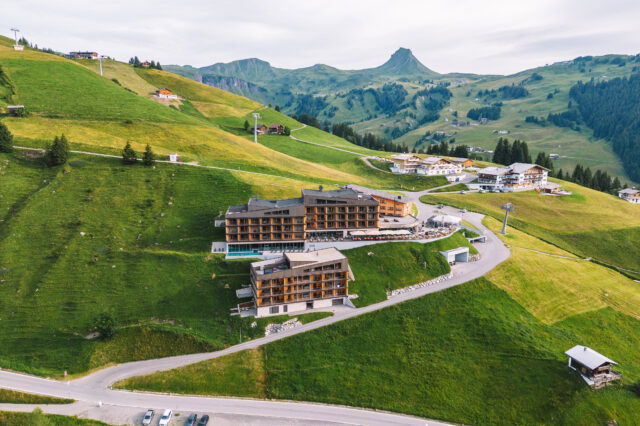 Ein Hotelkomplex auf einem Berg in Vorarlberg mit Pool und viel Holz.