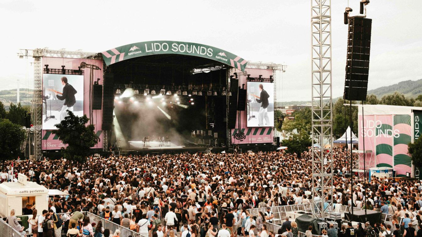 (c) Simone Grübl | Lido Sounds Großes Musikfestival LIDO SOUNDS 2025 in Linz mit Menschenmenge vor der Hauptbühne, Live-Konzert auf der Bühne mit LED-Leinwänden, Sommerstimmung, Festivalbesucher:innen und Bergen im Hintergrund – Open-Air-Event in Oberösterreich.