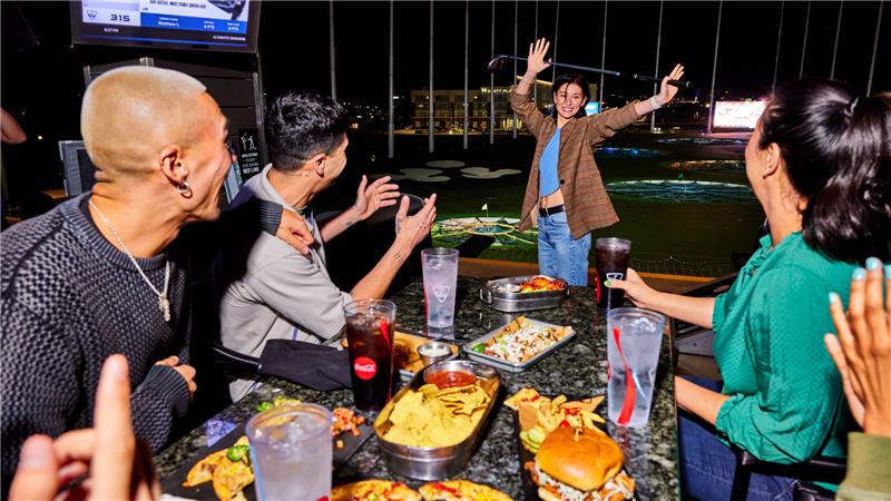 Eine Freundesgruppe feiert mit amerikanischen Snacks und Getränken bei Topgolf Wien.