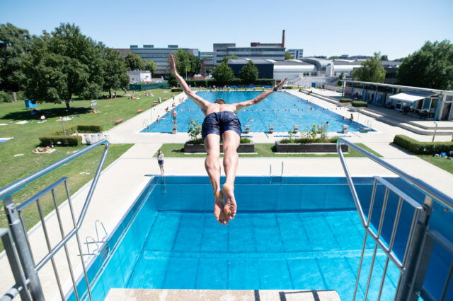 Eine Person springt im Parkbad Linz von einem Sprungturm ins Becken