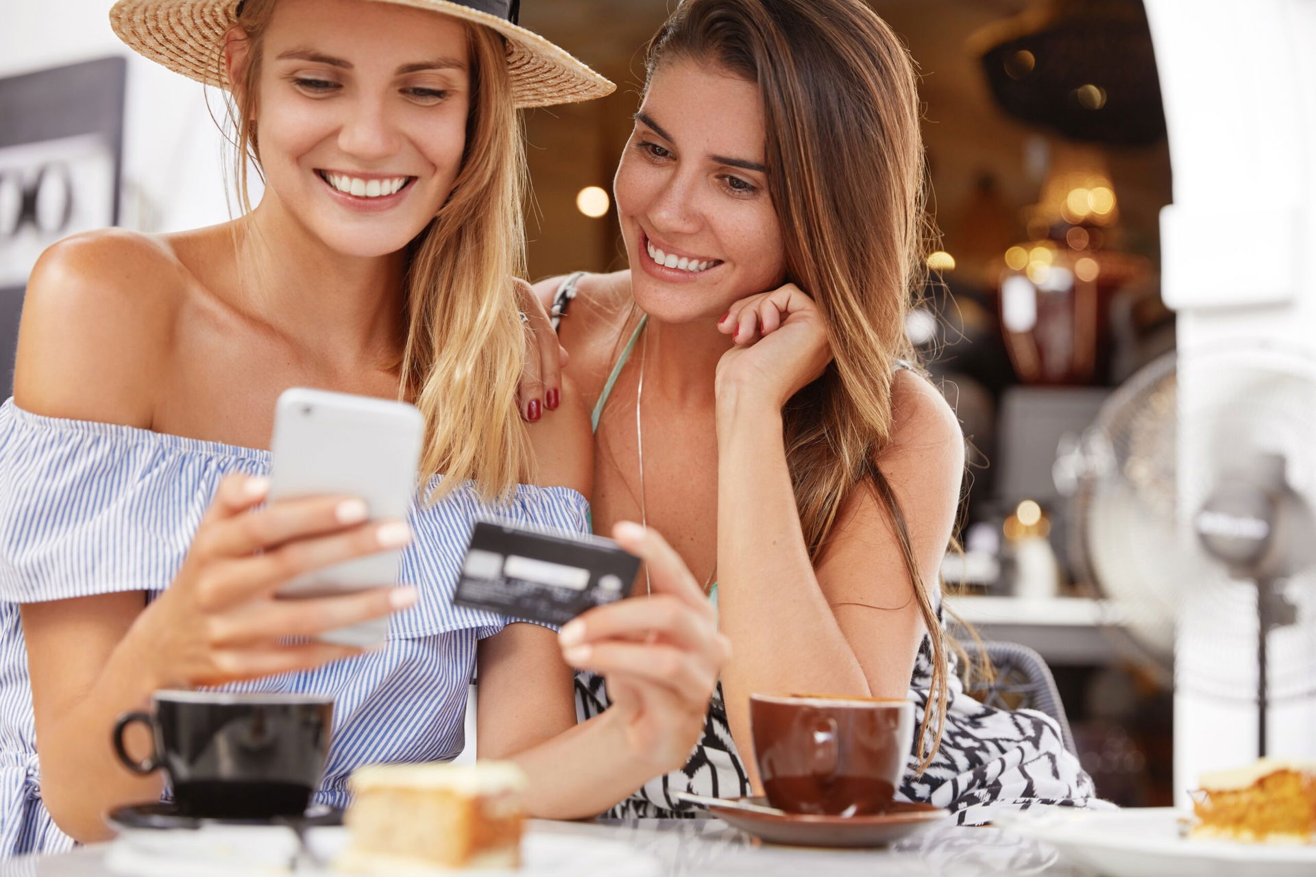 Zwei Frauen sitzen im Café und bezahlen online mit Kreditkarte und dem Handy