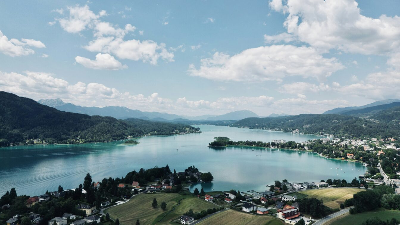 Blick auf einen kleinen Ort am See mit hügeliger Landschaft im Hintergrund