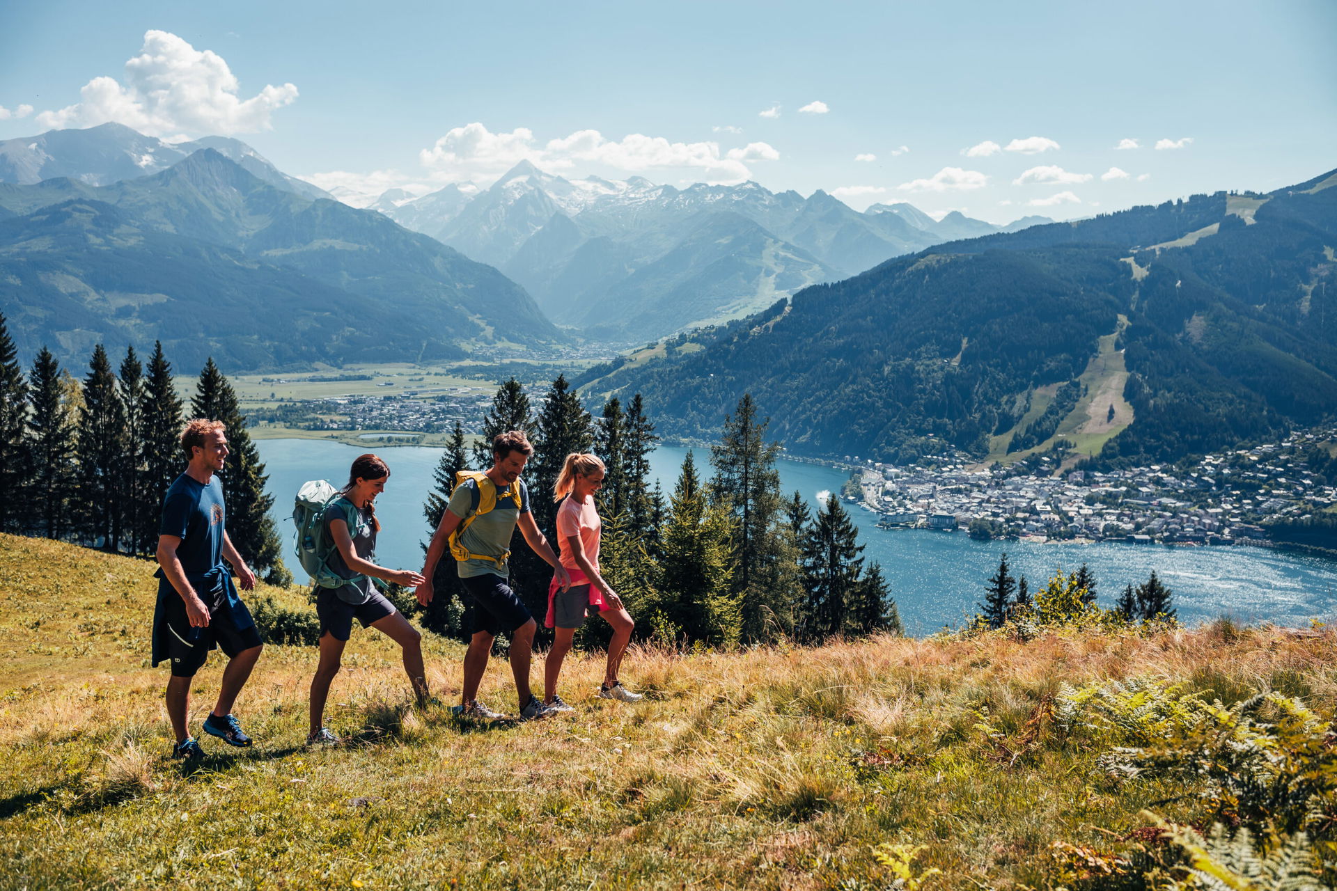 Vier Personen wandern in Zell am See-Kaprun. Die Landschaft ist herbstlich und der Zeller See ist im Hintergrund zu sehen.