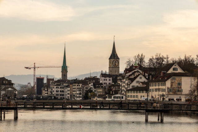 (c) Sonja Koller | 100things Blick auf das Panorama einer Stadt mit Fluss im Vordergrund und Bergen im Hintergrund.