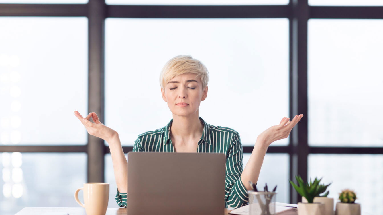 (c) AdobeStock_327312795 Meditation auf der Arbeit, eine Geschäftsfrau entspannt vor dem Laptop.